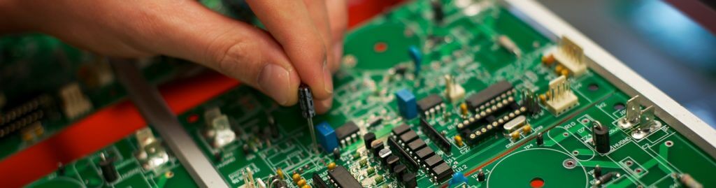 A hand working on an electronic circuit board.